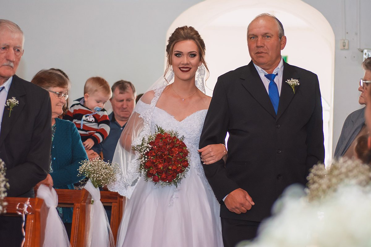 Noiva entrando na igreja acompanhada pelo seu pai no dia do seu casamento. Foto por Marco Moscarelli Fotografo Pelotas.