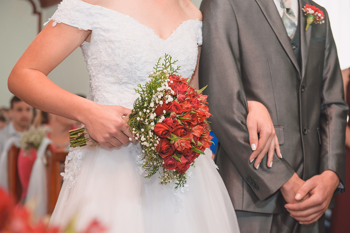 Fotografia em detalhe dos noivos de braços dados e com enfase no buquê da noiva. Foto por Marco Moscarelli Fotografo Pelotas.