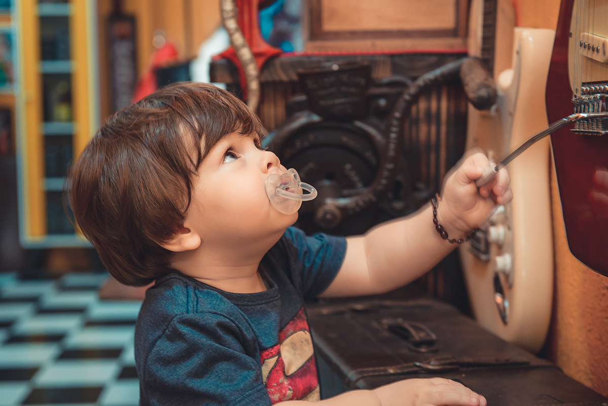 Bebê brincando com guitarra durante ensaio fotográfico de família. Foto por Marco Moscarelli Fotografo Pelotas.