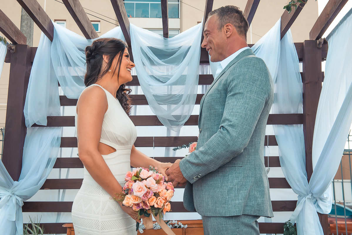 Noivos de mãos dadas durante a cerimonia de casamento. Retoques finais da maquiagem da noiva momentos antes do casamento. Foto por Marco Moscarelli Fotógrafo Pelotas.