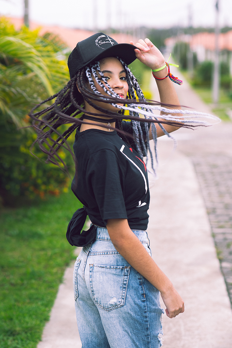 Modelo posando com boné  preto e jeans durante tendo sentada na rua verdes  seu ensaio fotográfico Tumblr em Pelotas. Foto por Marco Moscarelli Fotógrafo Pelotas.