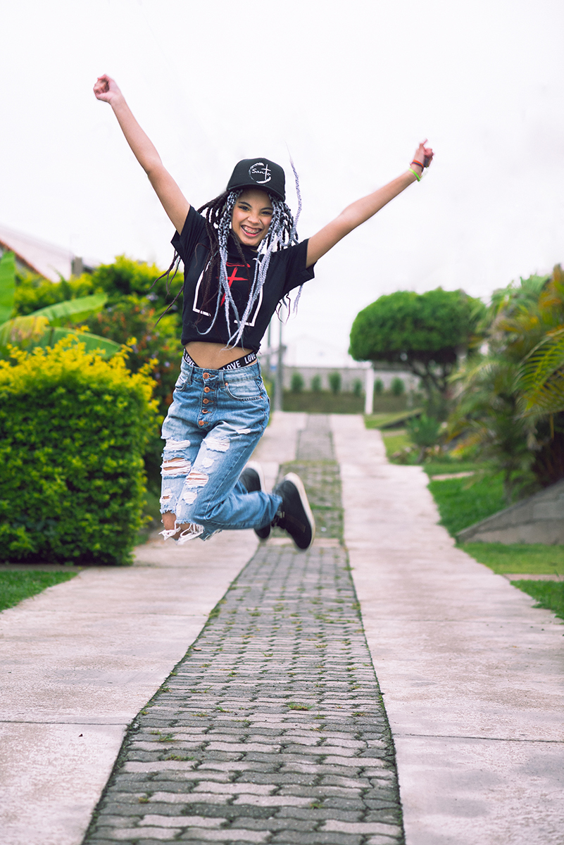 Modelo posando com boné  preto e jeans durante tendo sentada na rua verdes  seu ensaio fotográfico Tumblr em Pelotas. Foto por Marco Moscarelli Fotógrafo Pelotas.