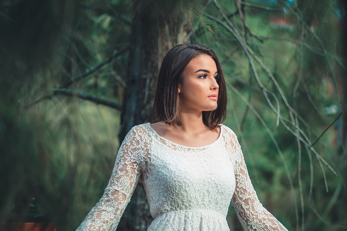 Linda fotografia da debutante em meio as arvores com um vestido branco durante seu ensaio fotográfico externo de 15 anos em Pelotas.  Foto por Marco Moscarelli Fotógrafo Pelotas.