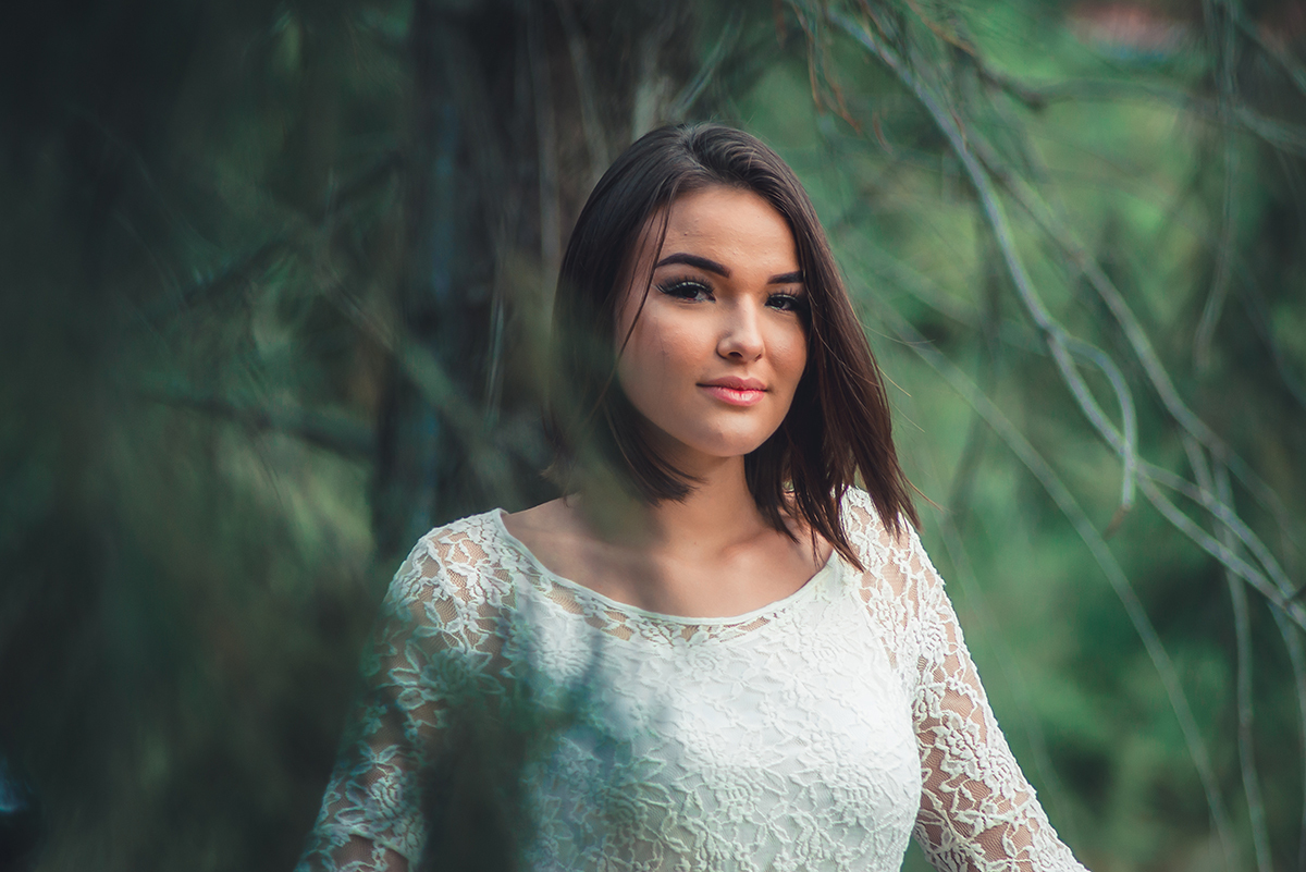 Linda fotografia da debutante em meio as arvores com um vestido branco durante seu ensaio fotográfico externo de 15 anos em Pelotas.  Foto por Marco Moscarelli Fotógrafo Pelotas.