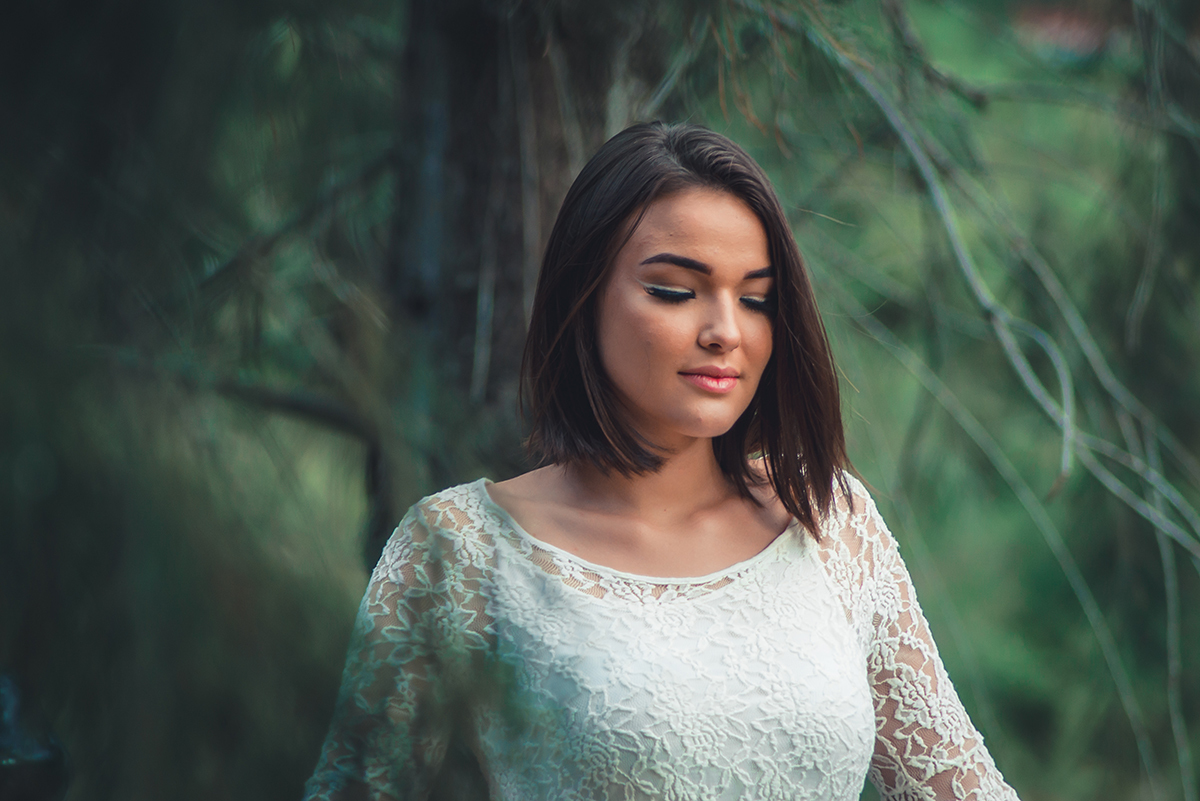 Linda fotografia da debutante em meio as arvores com um vestido branco durante seu ensaio fotográfico externo de 15 anos em Pelotas.  Foto por Marco Moscarelli Fotógrafo Pelotas.