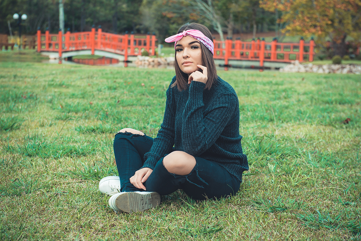 Debutante posando para foto sentada em um lindo campo verde durante seu ensaio externo de 15 anos. Foto por Marco Moscarelli Fotógrafo.