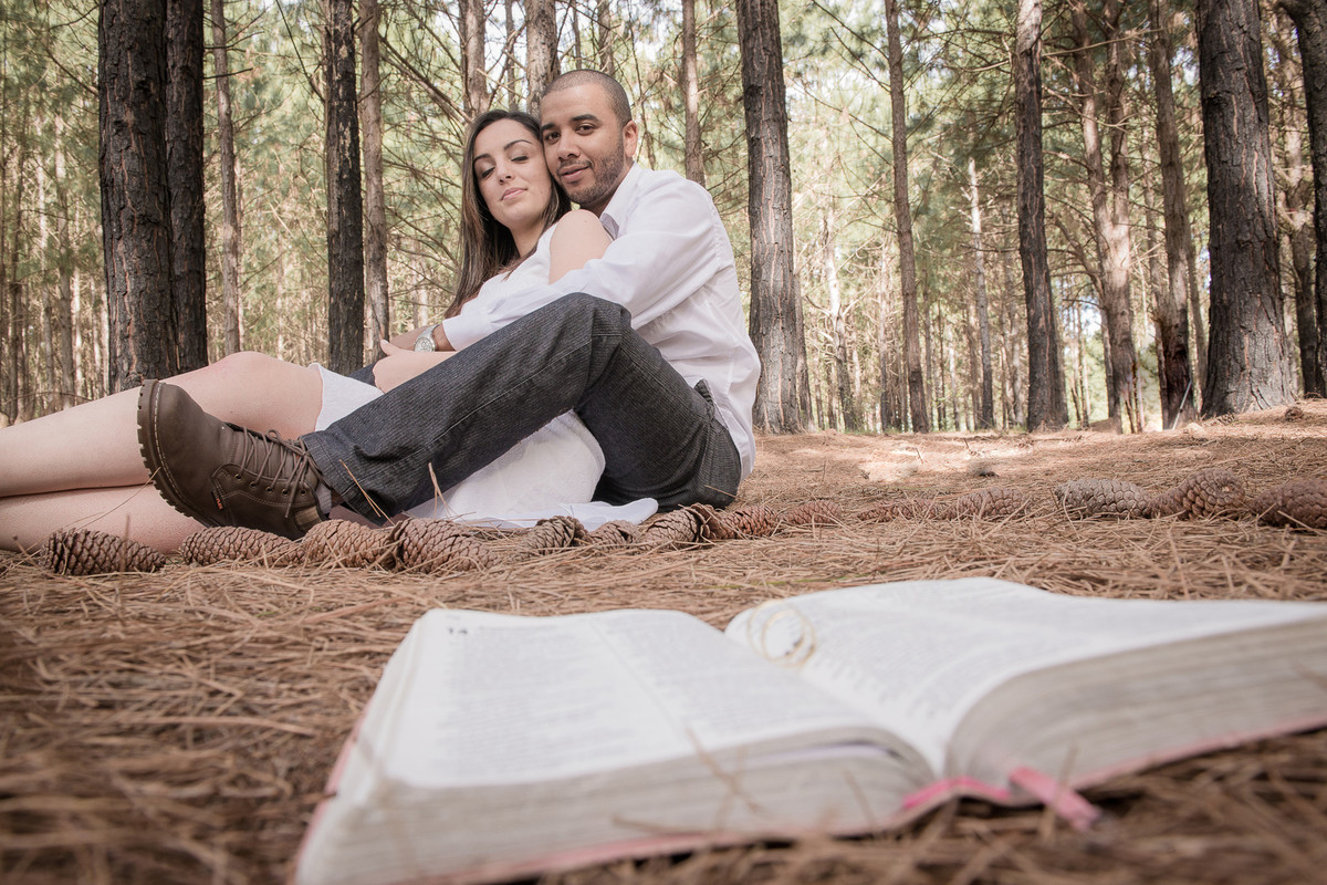 Casal de noivos posando para foto em lindo bosque com a biblia e as aliças compondo a cena.