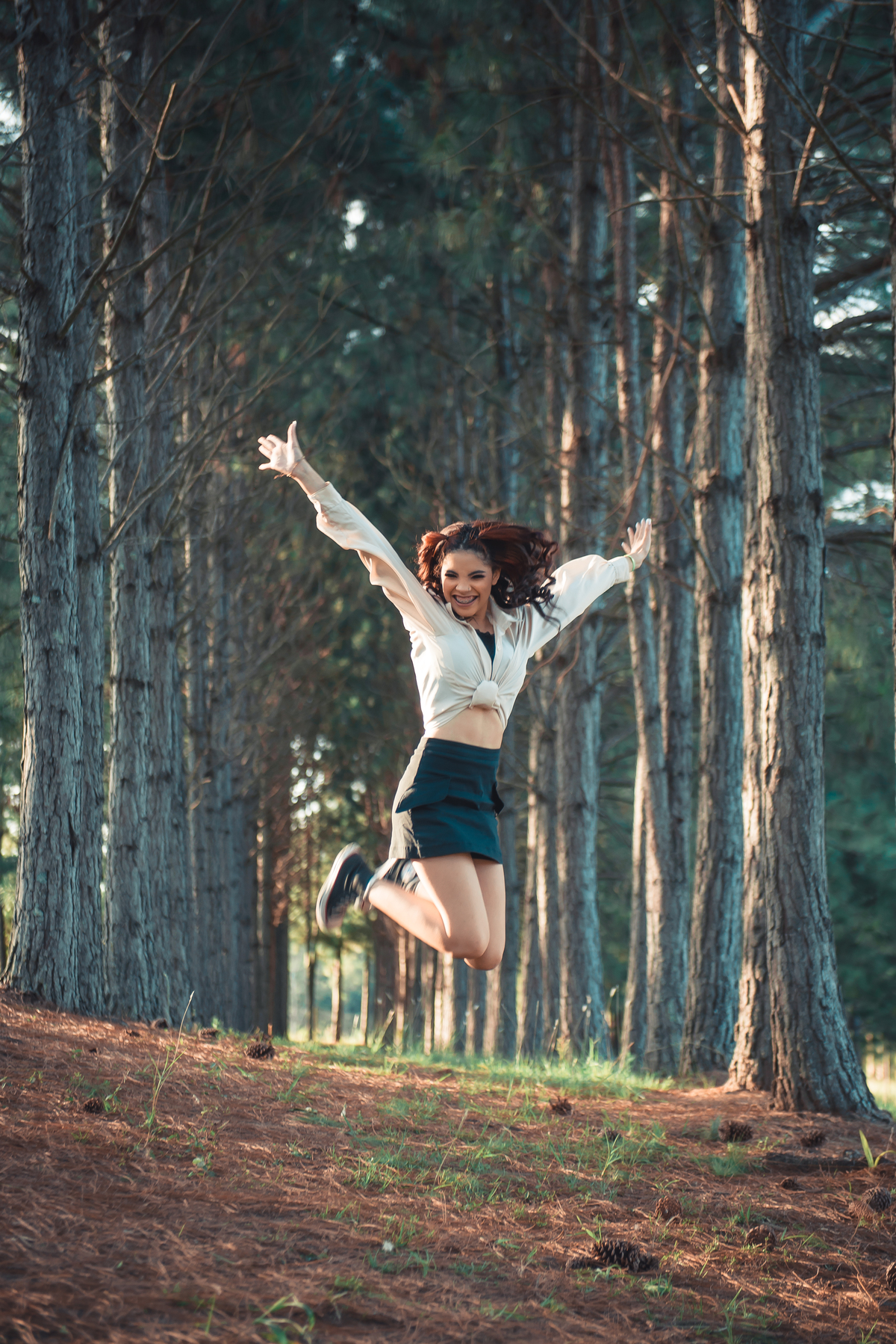Debutante saltando com joelhos dobrados durante seu ensaio fotográfico de 15 anos. Foto por Marco Moscarelli Fotógrafo Pelotas. 
