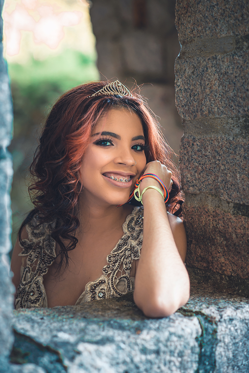 Debutante fotografada sorrindo alegre em uma janela de pedra de castelo durante seu ensaio fotográfico de 15 anos.  Foto por Marco Moscarelli 