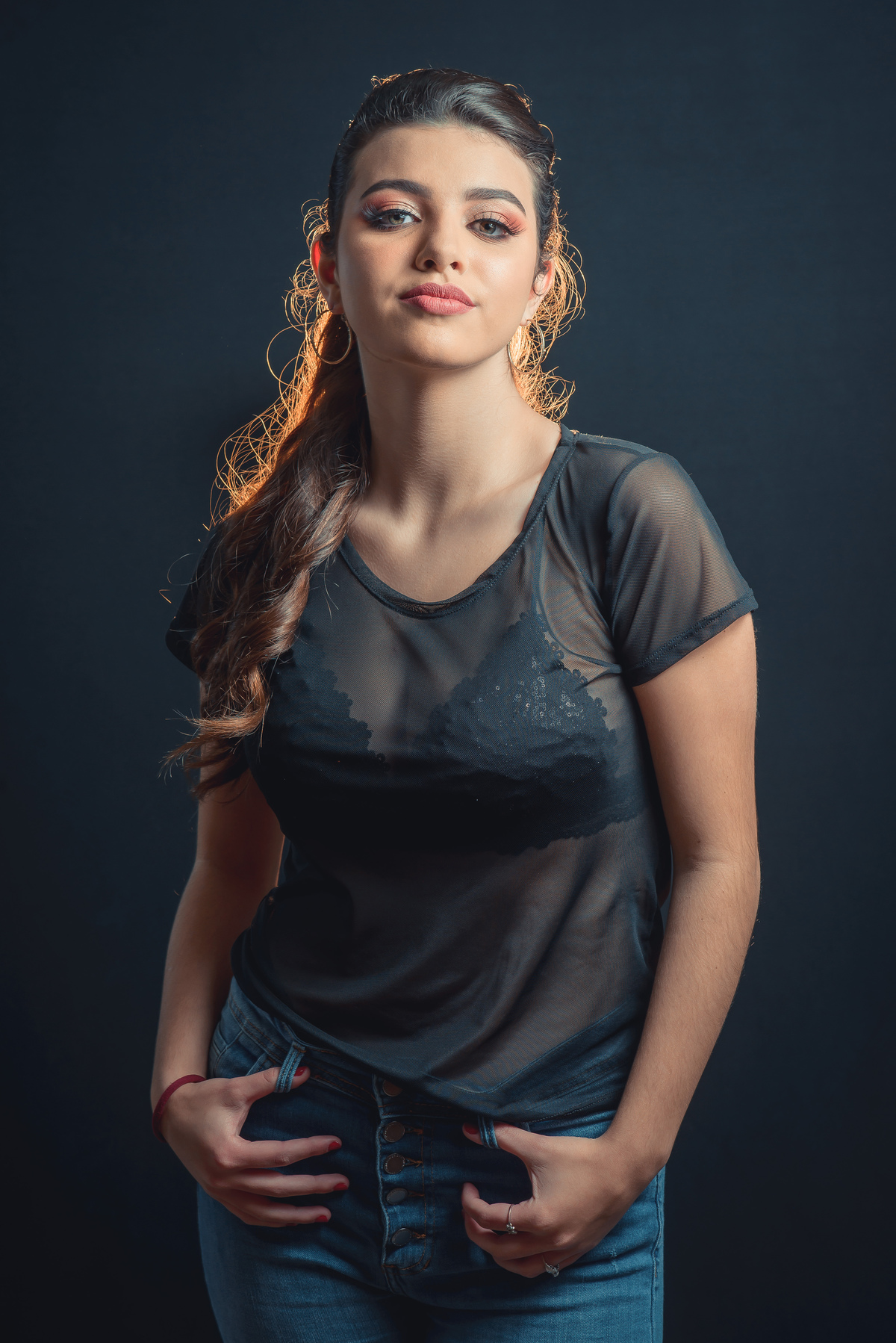 Modelo posando em estúdio com fundo preto usando uma blusa preta transparente e calça jeans. Olhos verdes chamando atenção neste lindo editorial de moda em estúdio fotográfico. Foto por Marco Moscarelli Fotógrafo Pelotas.