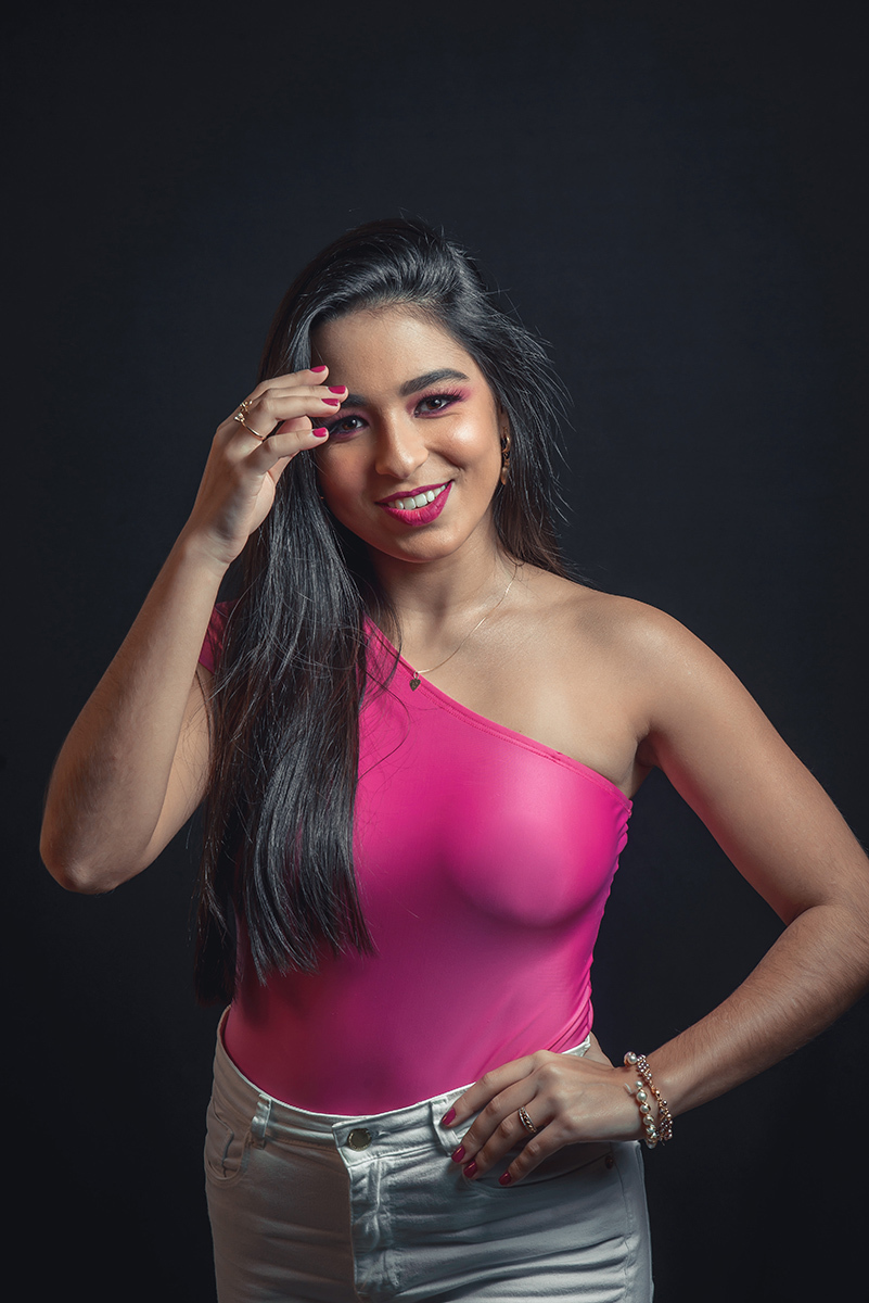 Modelo posando em estúdio com fundo preto usando uma blusa rosa e calça jeans branca. Olhos verdes chamando atenção neste lindo editorial de moda em estúdio fotográfico. Foto por Marco Moscarelli Fotógrafo Pelotas. 