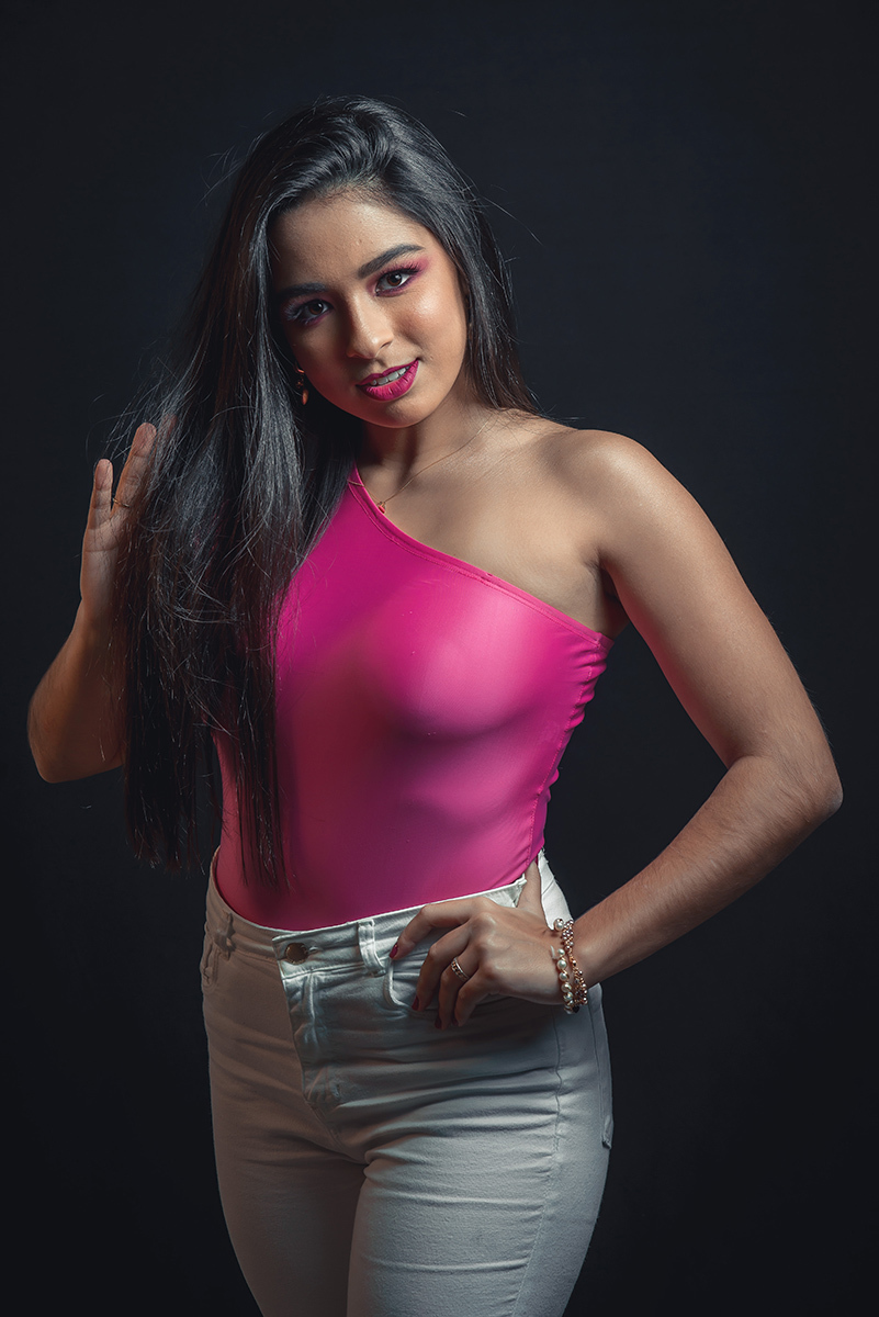 Modelo posando em estúdio com fundo preto usando uma blusa rosa e calça jeans branca. Olhos verdes chamando atenção neste lindo editorial de moda em estúdio fotográfico. Foto por Marco Moscarelli Fotógrafo Pelotas. 