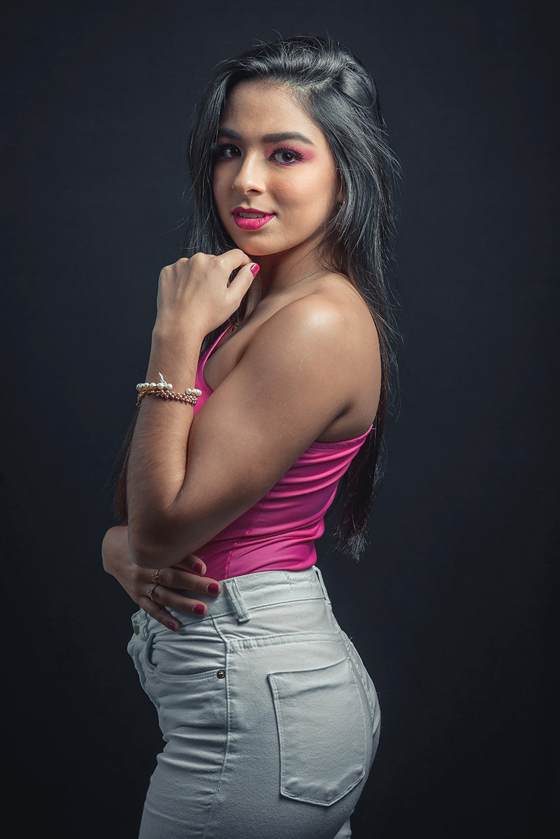 Modelo posando em estúdio com fundo preto usando uma blusa rosa e calça jeans branca. Olhos verdes chamando atenção neste lindo editorial de moda em estúdio fotográfico. Foto por Marco Moscarelli Fotógrafo Pelotas. 