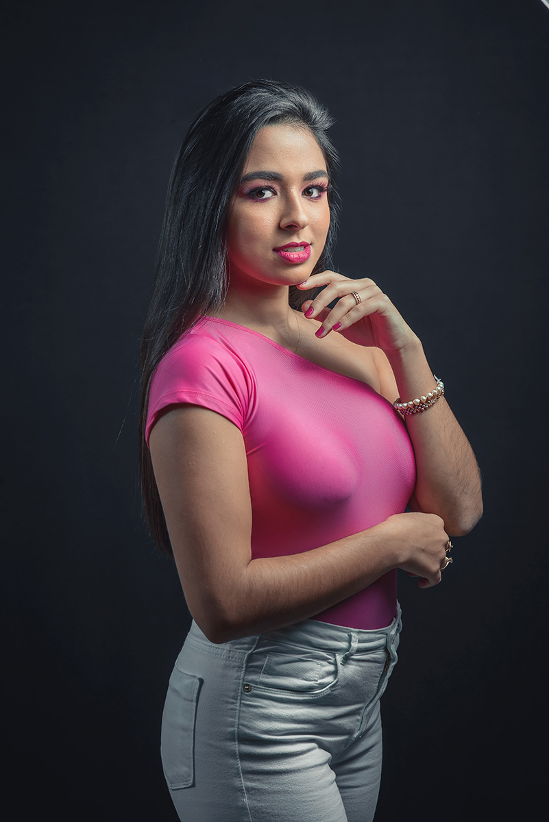 Modelo posando em estúdio com fundo preto usando uma blusa rosa e calça jeans branca. Olhos verdes chamando atenção neste lindo editorial de moda em estúdio fotográfico. Foto por Marco Moscarelli Fotógrafo Pelotas. 