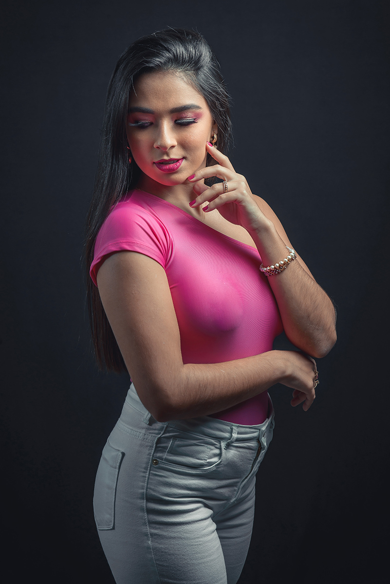 Modelo posando em estúdio com fundo preto usando uma blusa rosa e calça jeans branca. Olhos verdes chamando atenção neste lindo editorial de moda em estúdio fotográfico. Foto por Marco Moscarelli Fotógrafo Pelotas. 