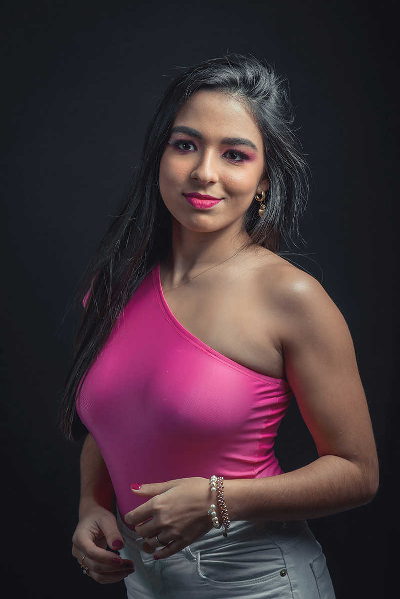 Modelo posando em estúdio com fundo preto usando uma blusa rosa e calça jeans branca. Olhos verdes chamando atenção neste lindo editorial de moda em estúdio fotográfico. Foto por Marco Moscarelli Fotógrafo Pelotas. 