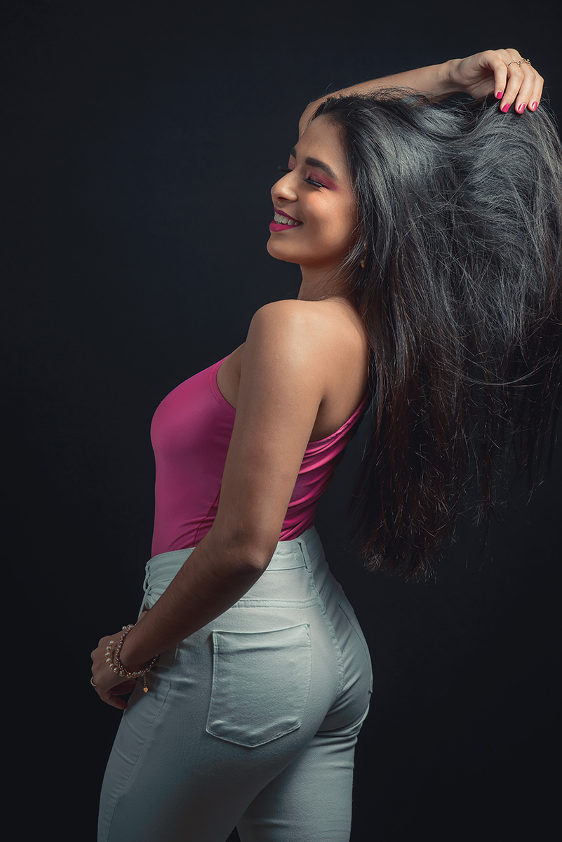 Modelo posando em estúdio com fundo preto usando uma blusa rosa e calça jeans branca. Olhos verdes chamando atenção neste lindo editorial de moda em estúdio fotográfico. Foto por Marco Moscarelli Fotógrafo Pelotas. 