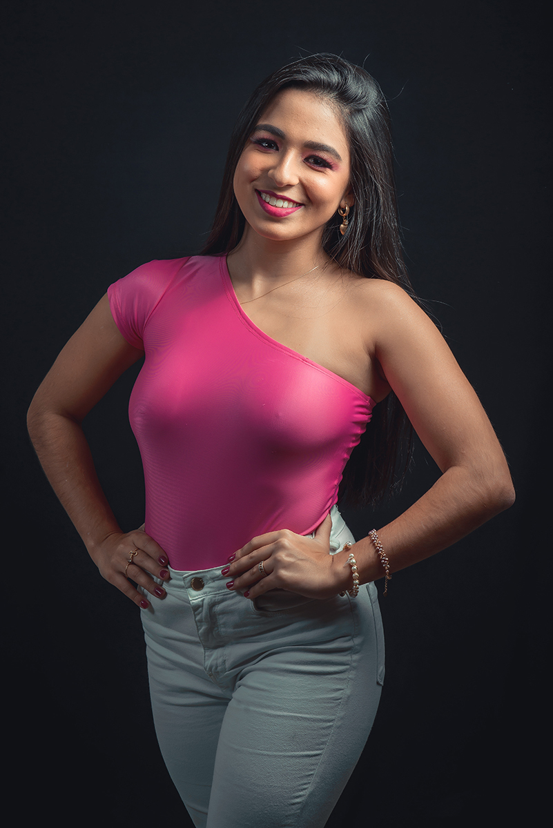 Modelo posando em estúdio com fundo preto usando uma blusa rosa e calça jeans branca. Olhos verdes chamando atenção neste lindo editorial de moda em estúdio fotográfico. Foto por Marco Moscarelli Fotógrafo Pelotas. 