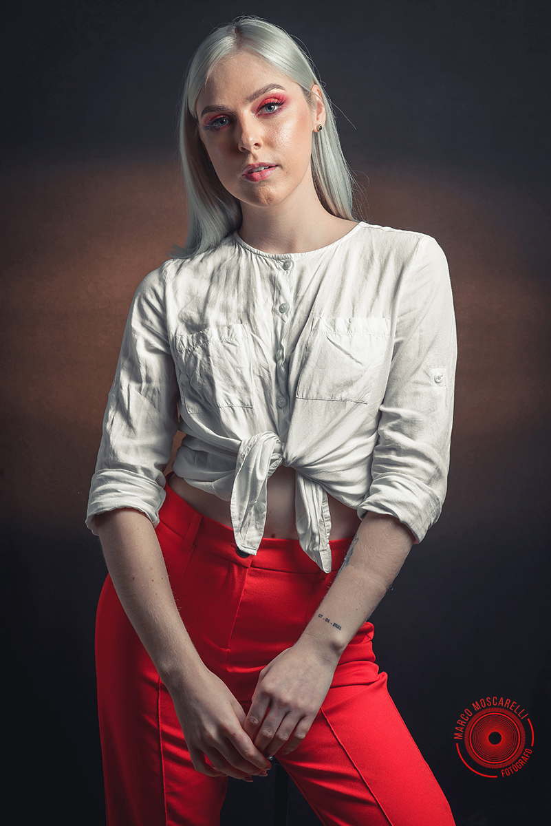 Modelo posando em fundo Preto usando uma calça vermelha e blusinha branca em editorial de moda em estúdio fotográfico. Foto por Marco 