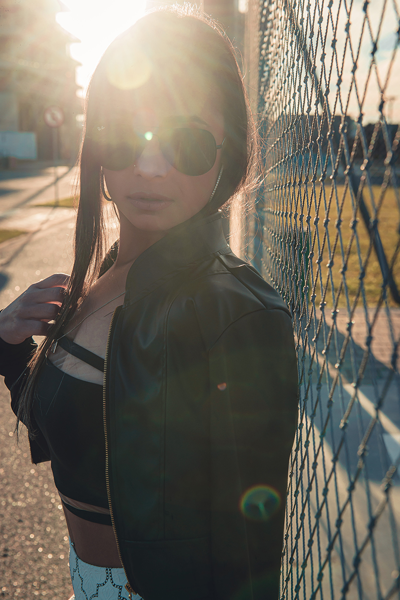 Modelo posando  encostada em tela de quadra de esportes, usando roupas despojadas  em ensaio fotográfico  durante o por do sol realizado no parque Una em Pelotas. Foto por Marco Moscarelli Fotógrafo Pelotas.