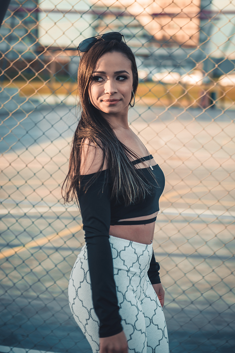Modelo posando  encostada em tela de quadra de esportes, usando roupas despojadas  em ensaio fotográfico realizado no parque Una em Pelotas. Foto por Marco Moscarelli Fotógrafo Pelotas.