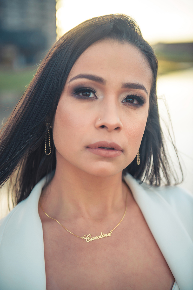 Modelo posando com a mão no cabelo e usando um terninho branco para fotografia com o fundo desfocado em ensaio fotográfico realizado no parque Una em Pelotas. Foto por Marco Moscarelli Fotógrafo Pelotas.