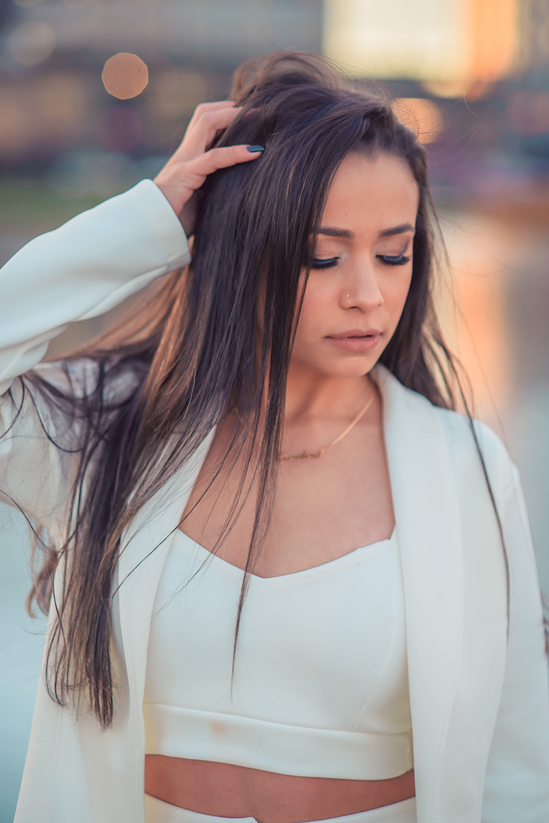 Modelo posando com a mão no cabelo e usando um terninho branco para fotografia em ensaio fotográfico realizado no parque Una em Pelotas. Foto por Marco Moscarelli Fotógrafo Pelotas.