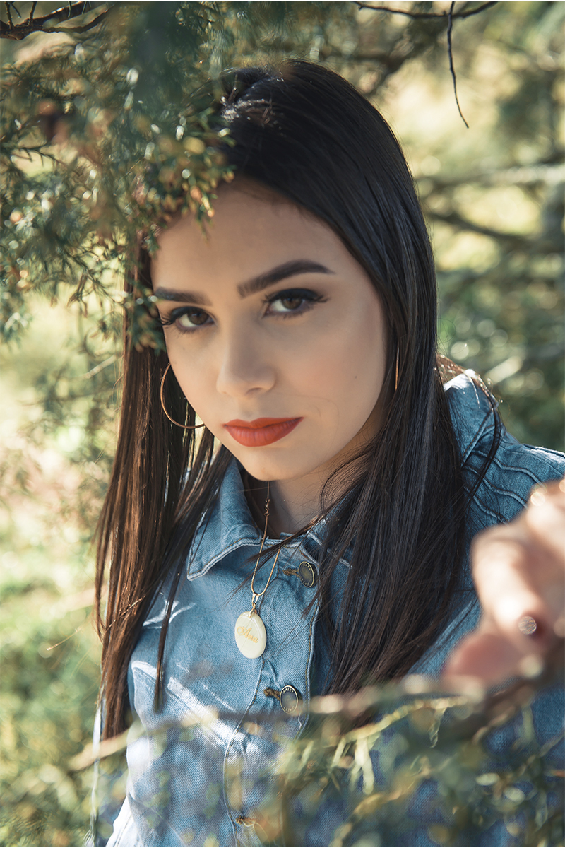 Retrato da debutante e aniversariante olhando por entre as árvores, durante seu ensaio de 15 anos para seu aniversário de 15 anos. Foto por Marco Moscarelli Fotógrafo Pelotas.  