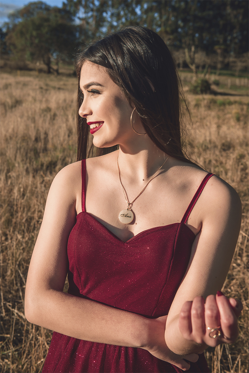 Debutante posando para foto em um campo amarelo com um lindo vestido vermelho e olhando para o sol, durante seu ensaio de 15 anos para seu aniversário de 15 anos. Foto por Marco Moscarelli 