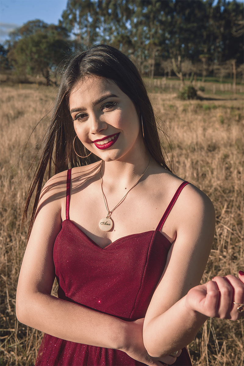 Debutante posando para foto em um campo amarelo com um lindo vestido vermelho e olhando para o sol, durante seu ensaio de 15 anos para seu aniversário de 15 anos. Foto por Marco Moscarelli 
