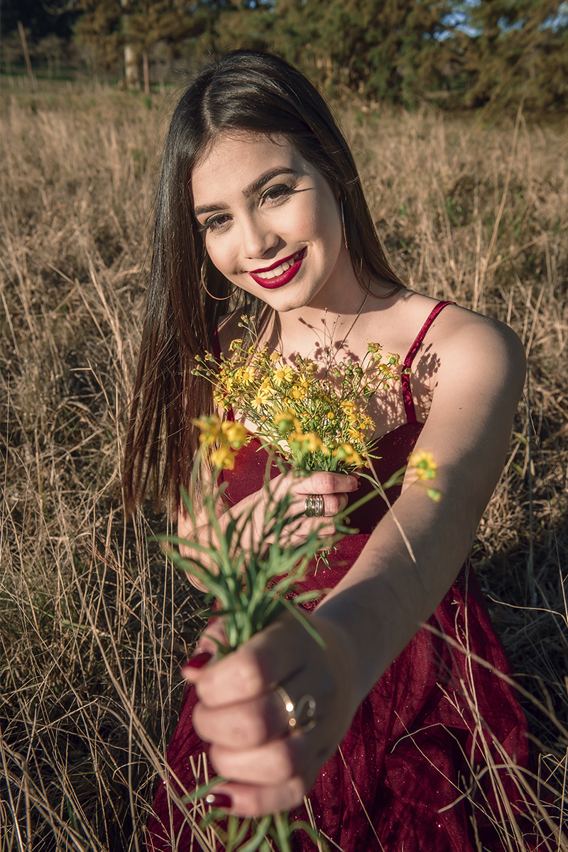 Debutante posando para foto com um buquê de flores amarelo em um campo amarelo com um lindo vestido vermelho 
