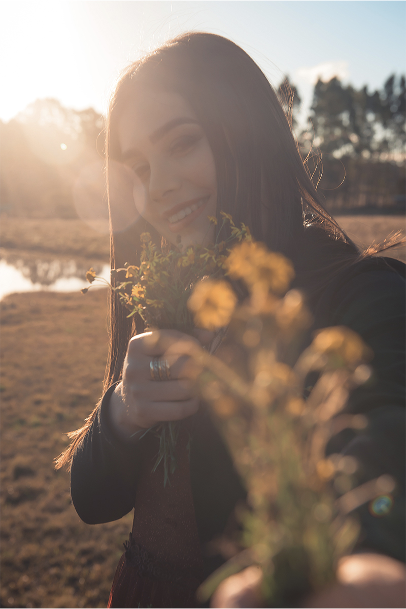 Debutante posando para foto com um buquê de flores amarelo em um campo amarelo com um lindo vestido vermelho 