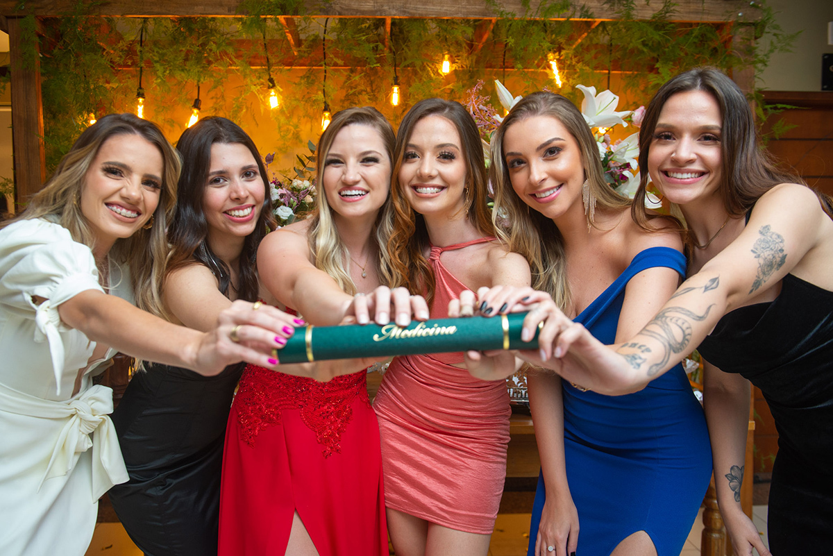 Fotografia divertida da formanda em medicina segurando o canudo com diploma de formatura durante a sua recepção de formatura em medicina. Lindo retrato da formanda no curso de medicina durante a recepção de formatura em medicina em Pelotas. Foto por Marco