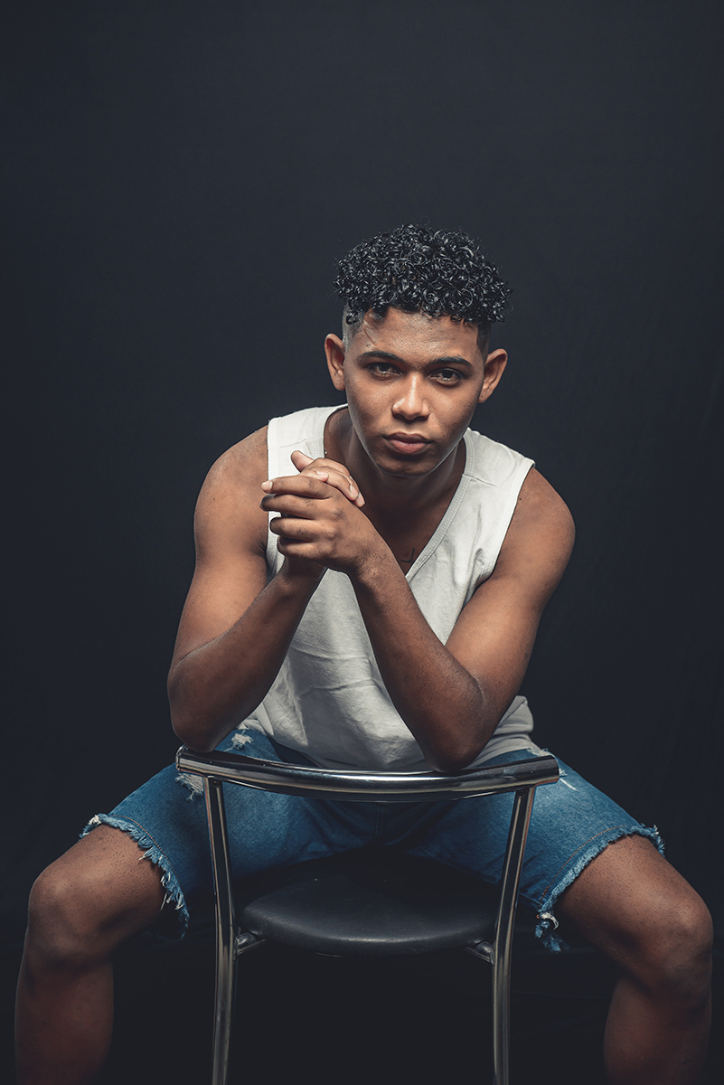 Modelo posando para foto colorida em estúdio com fundo preto, usando camiseta banca e bermuda. Foto por Marco Moscarelli Fotografo Pelotas.