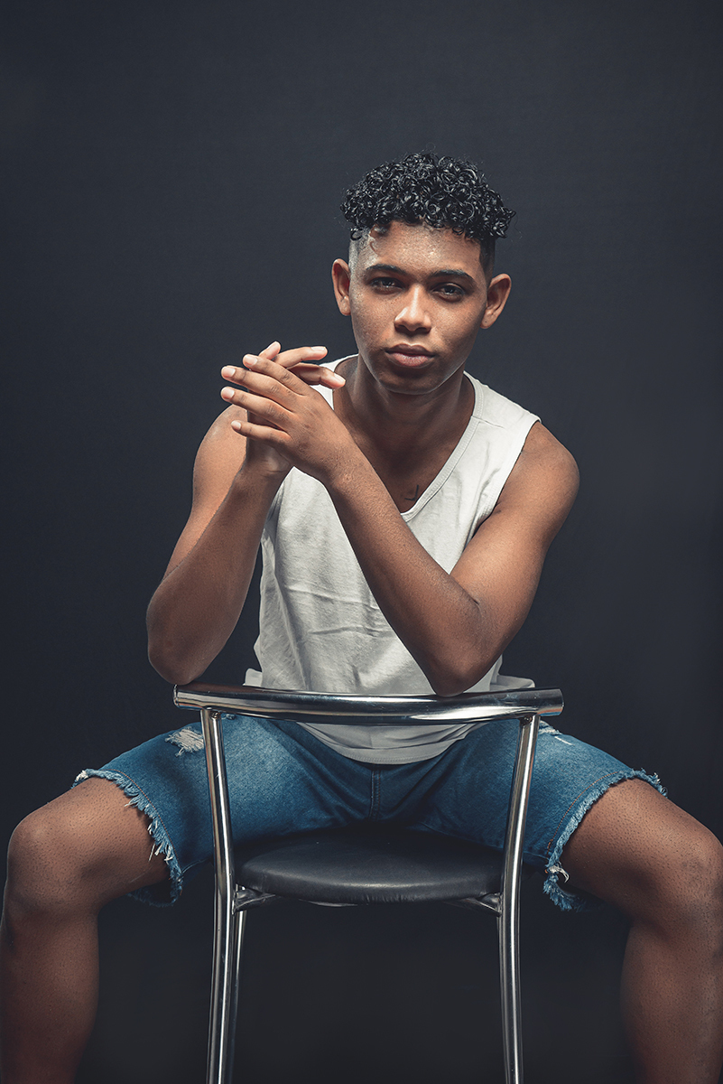 Modelo posando para foto colorida em estúdio com fundo preto, usando camiseta banca e bermuda. Foto por Marco Moscarelli Fotografo Pelotas.
