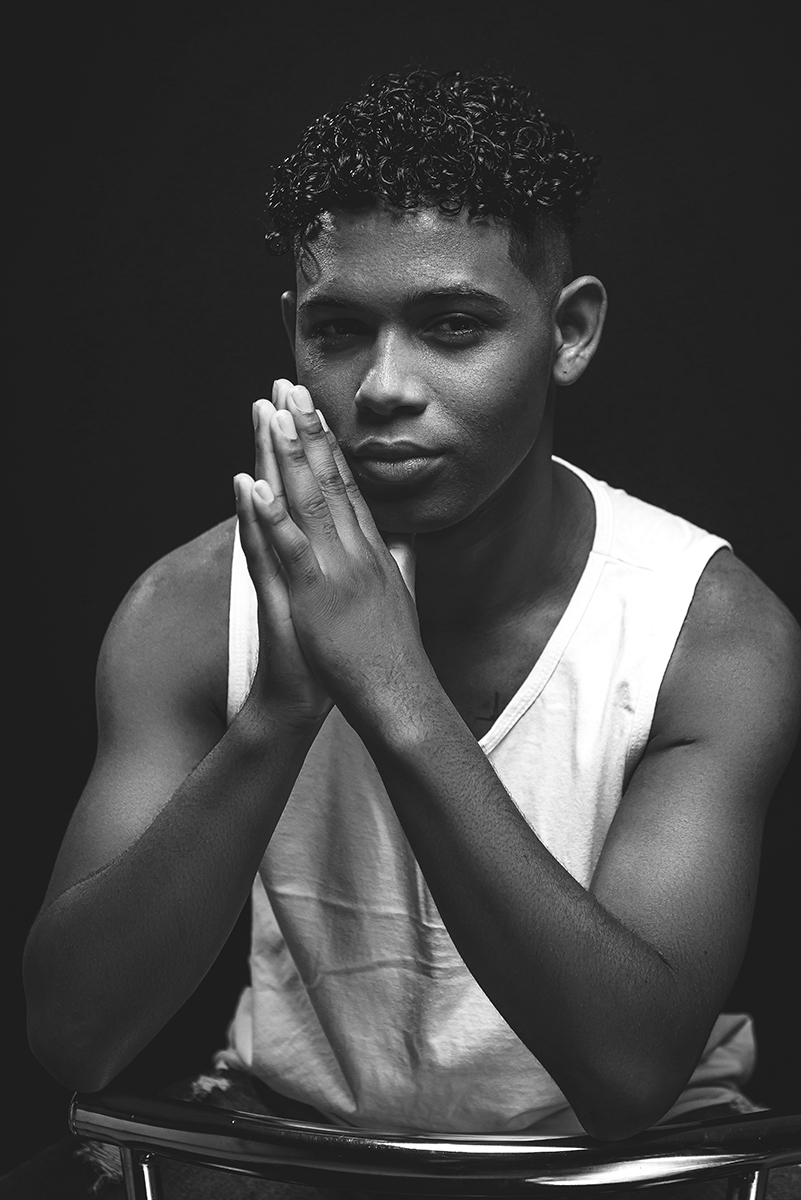Modelo posando para foto preto e branco  em estúdio com fundo preto, usando camiseta banca e bermuda. Foto por Marco Moscarelli Fotografo Pelotas.