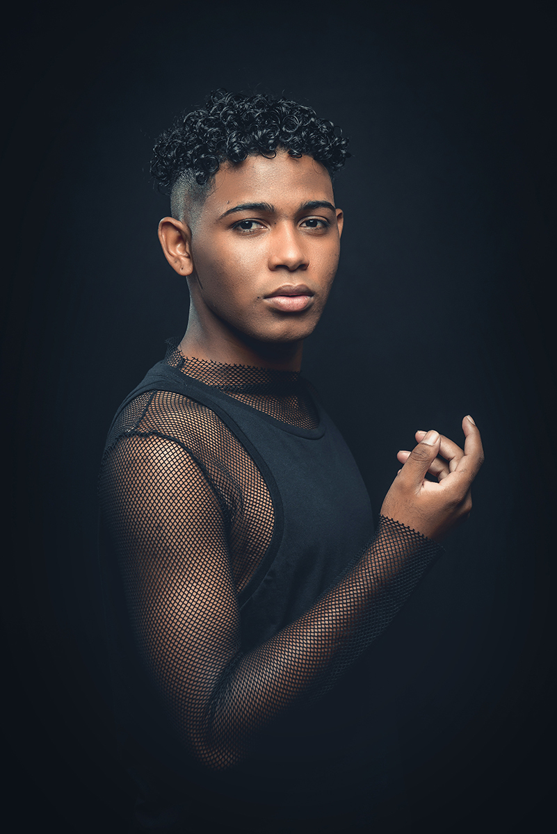 Modelo posando para foto colorida em estúdio com fundo preto, usando camiseta camisa e calça preta. Foto por Marco Moscarelli Fotografo Pelotas.