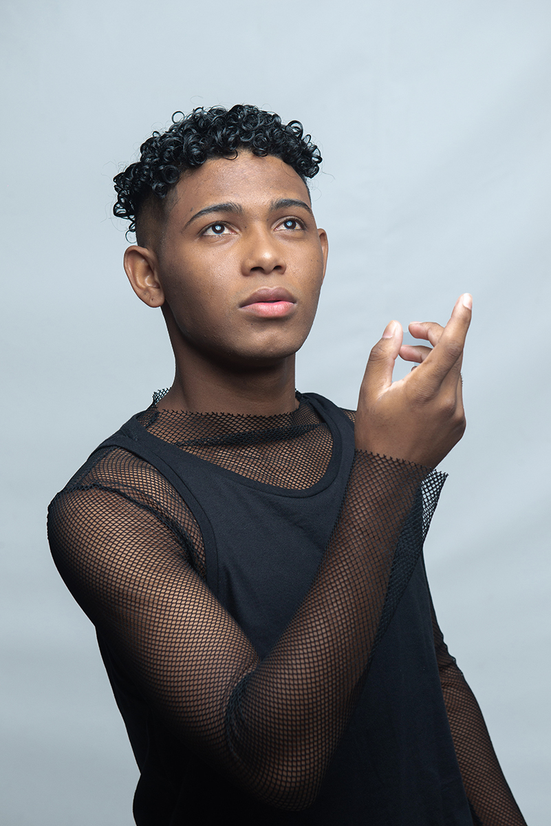 Modelo posando para foto colorida em estúdio com fundo branco, usando camiseta camisa e calça preta. Foto por Marco Moscarelli Fotografo Pelotas