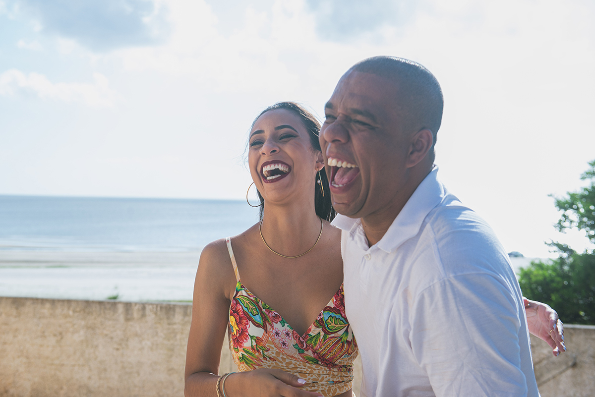 Casal sorrindo de alegria durante seu ensaio de casal pré wedding na praia da Capilha. Foto por Marco Moscarelli Fotógrafo Pelotas.