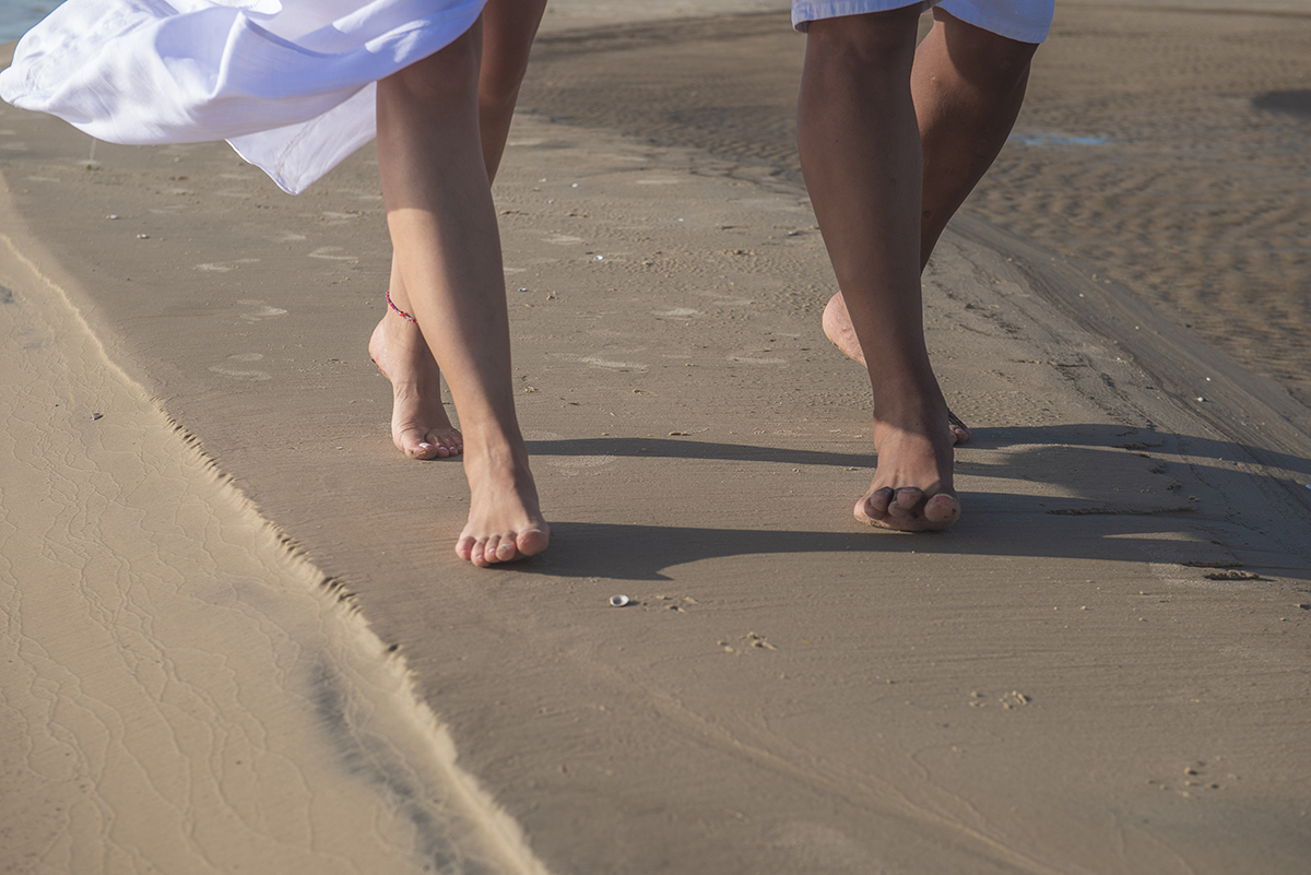 Foto em detalhe dos pés dos noivos caminhando pela praia durante seu ensaio de casal pré wedding. ensaio de casal na praia da caiplha. Foto por Marco Moscarelli Fotógrafo Pelotas