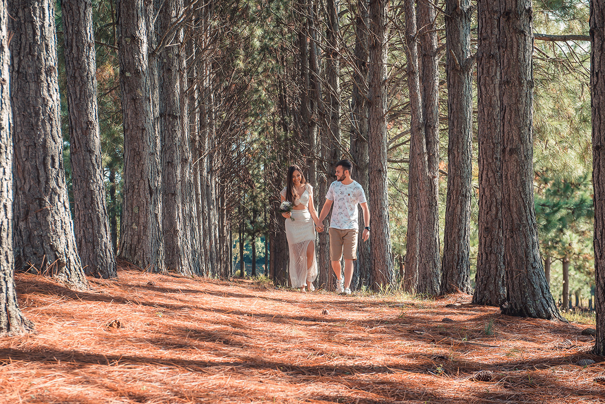 Fotografia dos noivos caminhando felizes por um bosque durante seu ensaio pré wedding no seu pré casamento na chácara Fiss. Foto por Marco Moscarelli Fotógrafo Pelotas.