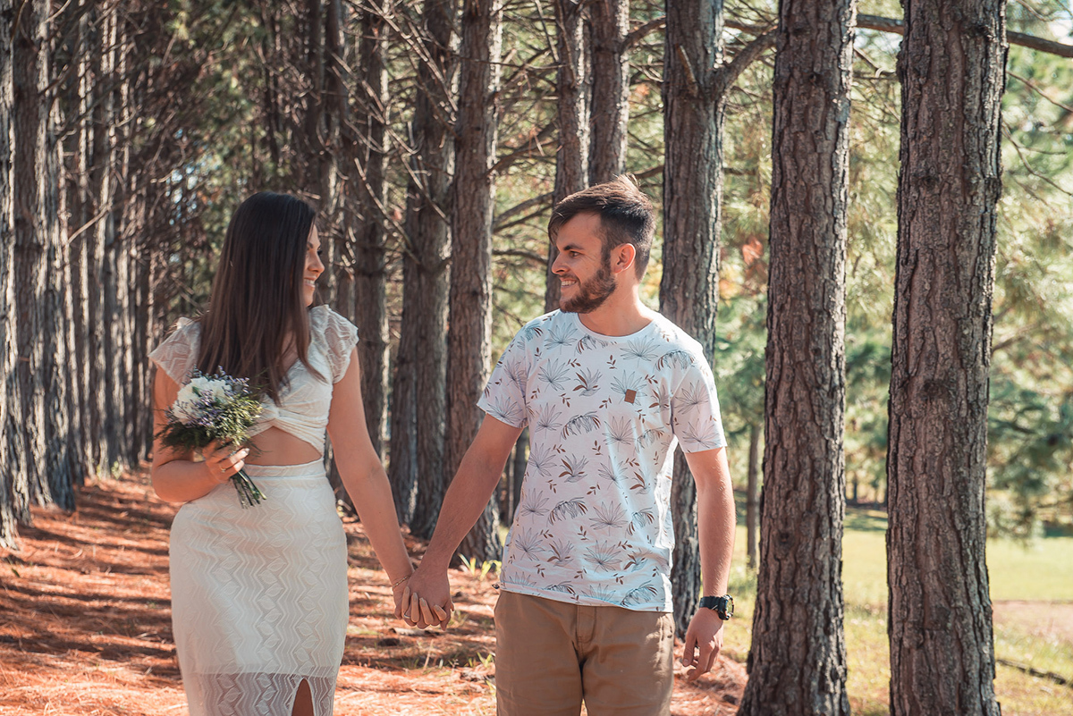 Fotografia dos noivos caminhando felizes por um bosque durante seu ensaio pré wedding no seu pré casamento na chácara Fiss. Foto por Marco Moscarelli Fotógrafo Pelotas.
