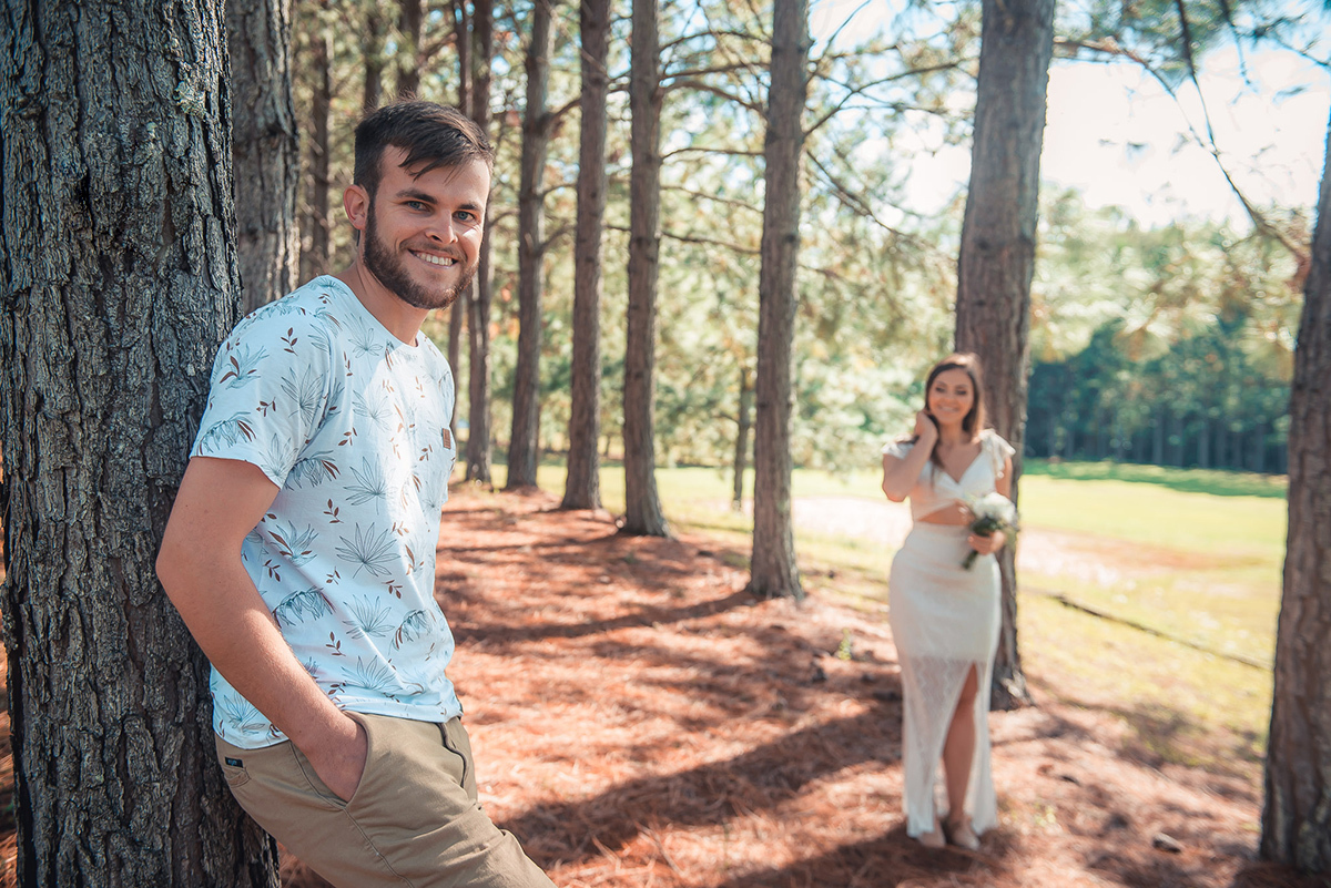 Fotografia do noivo sorrindo em momento descontraído sendo observado pela noiva durante seu ensaio pré wedding no seu pré casamento na chácara Fiss. Foto por Marco Moscarelli Fotógrafo Pelotas.