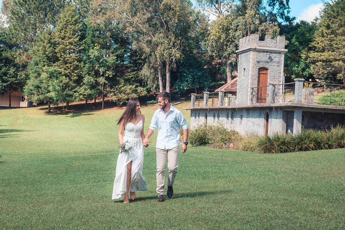 Noivos caminhando felizes por um lindo gramado verde com um castelo ao fundo durante seu ensaio pré wedding no seu pré casamento na chácara Fiss. Foto por Marco Moscarelli Fotógrafo Pelotas.