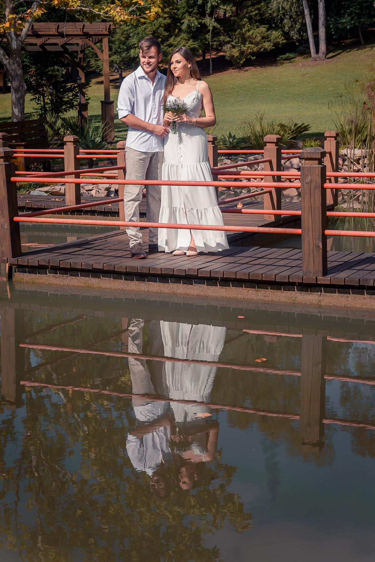 Fotografia do casal de noivos em uma ponte de um jardim japonês com ênfase no reflexo na agua  durante seu ensaio pré wedding no seu pré casamento na chácara Fiss. Foto por Marco Moscarelli Fotógrafo Pelotas. 