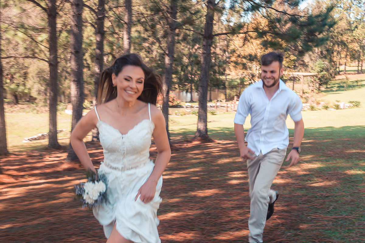 Casal de noivos posando para foto levemente desfocada correndo em um lindo gramado em meio a natureza durante seu ensaio pré wedding no seu pré casamento na chácara Fiss. Foto por Marco Moscarelli Fotógrafo Pelotas.