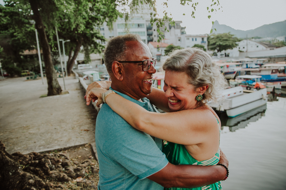 Fotografia afetiva de casal maduro rindo juntos na Mureta da Urca, RJ.