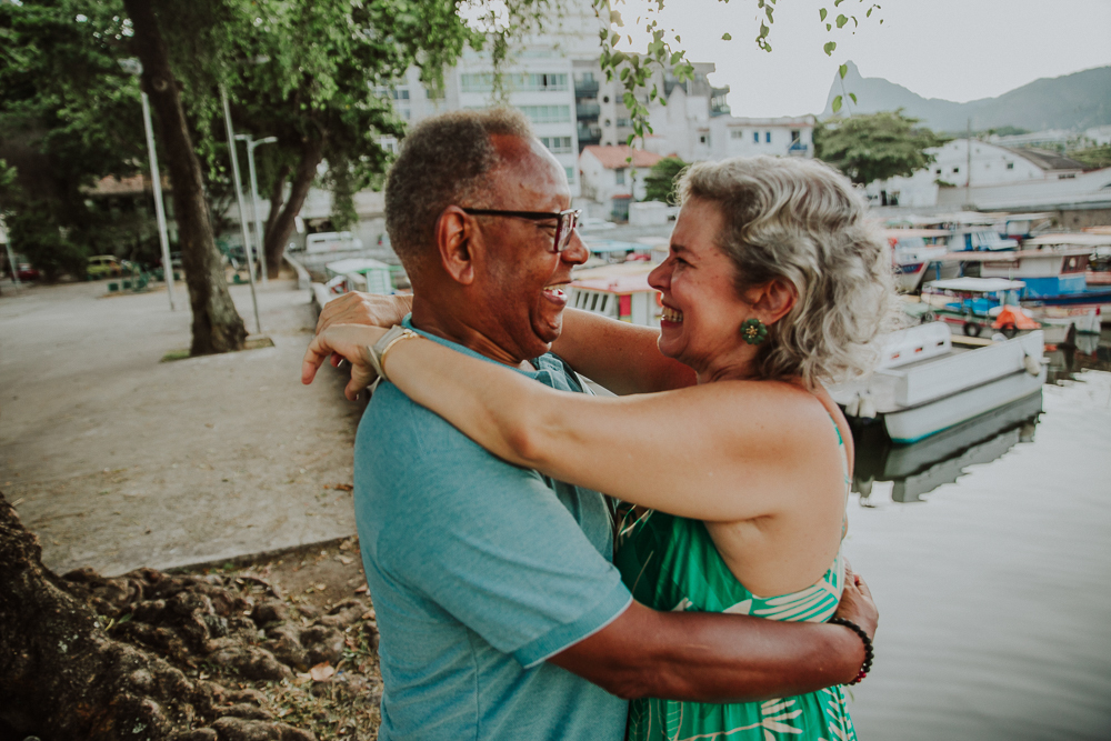 Casal maduro sorrindo e se abraçando durante ensaio fotográfico de aniversário de casamento na Mureta da Urca, Rio de Janeiro.