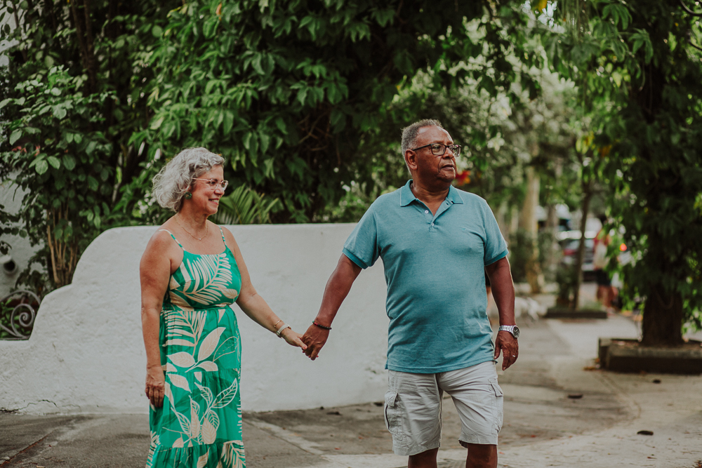 Fotografia afetiva de casal maduro caminhando de mãos dadas em rua arborizada do Rio de Janeiro.