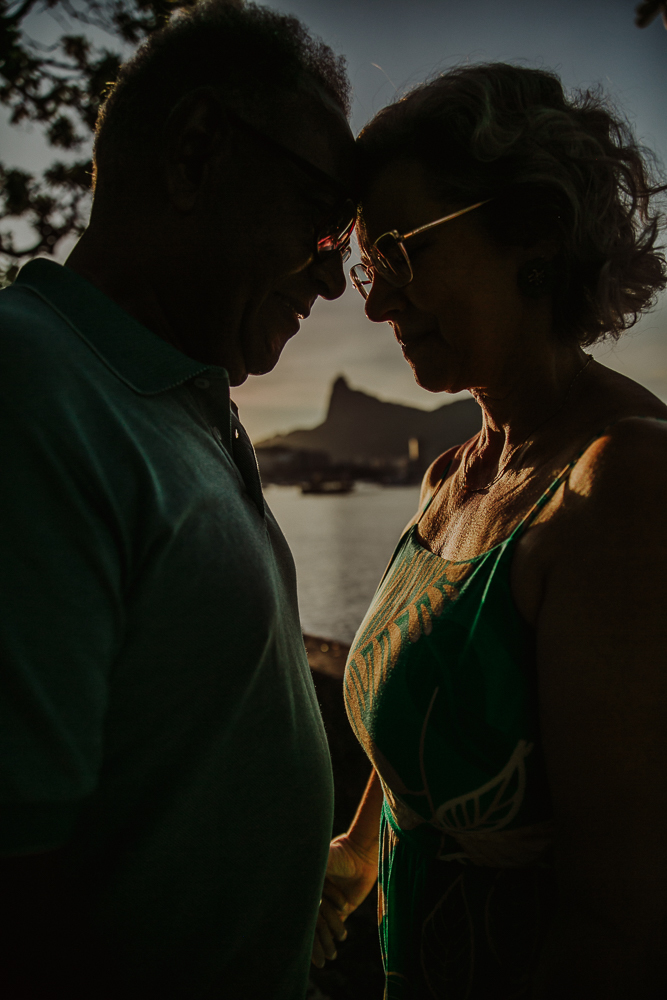  Casal maduro encostando testas em momento íntimo ao pôr do sol no Rio de Janeiro com vista para o Cristo Redentor na Mureta da Urca